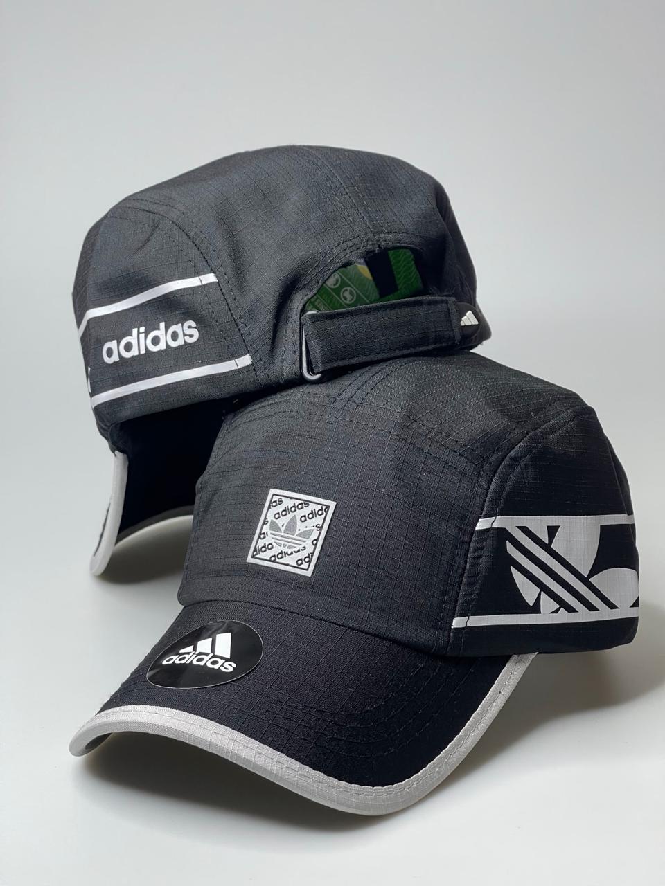 Boné preto Adidas esportivo com detalhes em cinza e logos da marca, fundo branco.