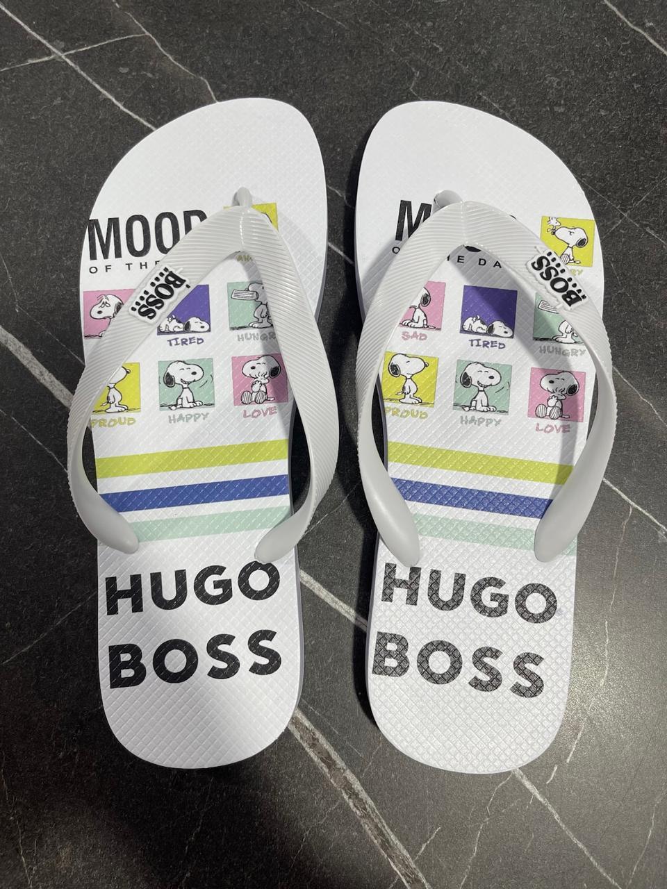 Chinelo HUGO BOSS branco com tiras brancas, estampas Snoopy e frases divertidas, em piso escuro.