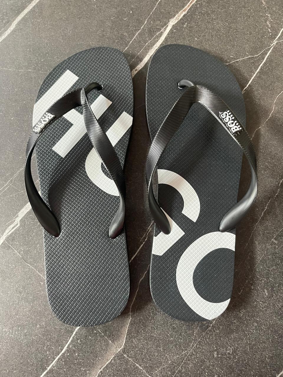 Chinelo Hugo Boss preto com tiras e logo branco em piso de pedra escura