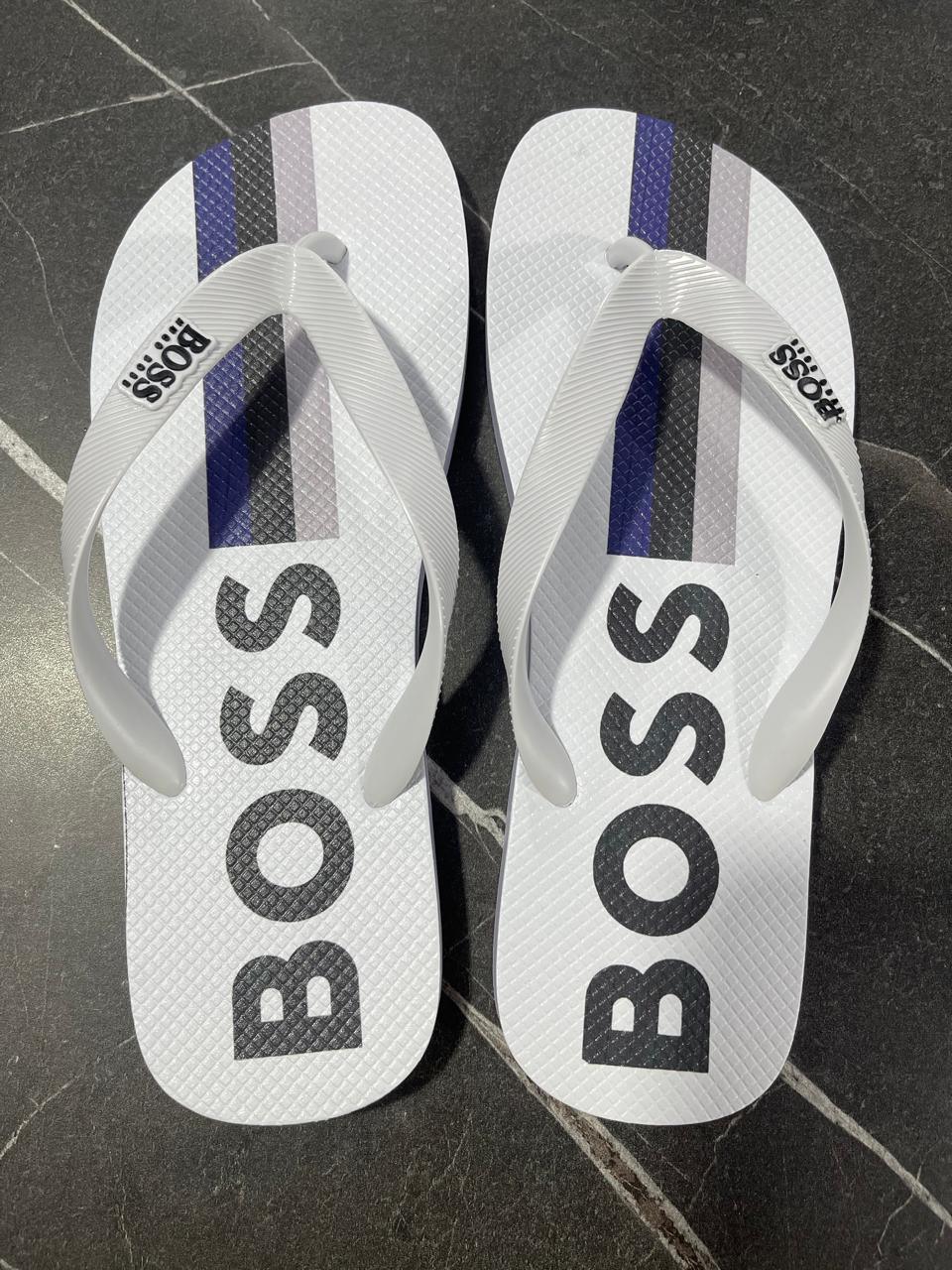 Chinelo Hugo Boss branco com listras e logo BOSS, sobre piso preto de mármore