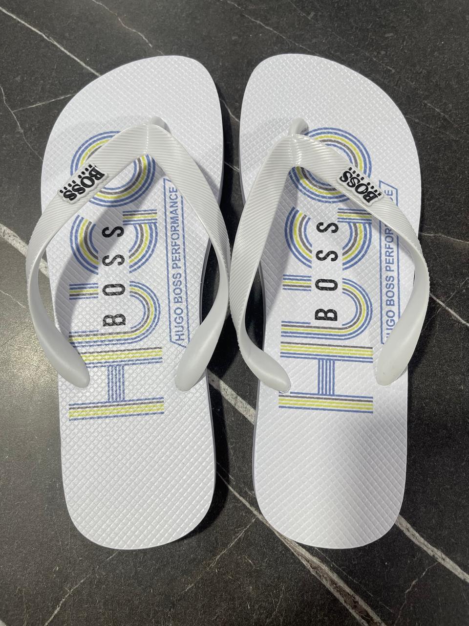 Chinelo branco Hugo Boss com logo colorido, tiras brancas, em piso de pedra escura.