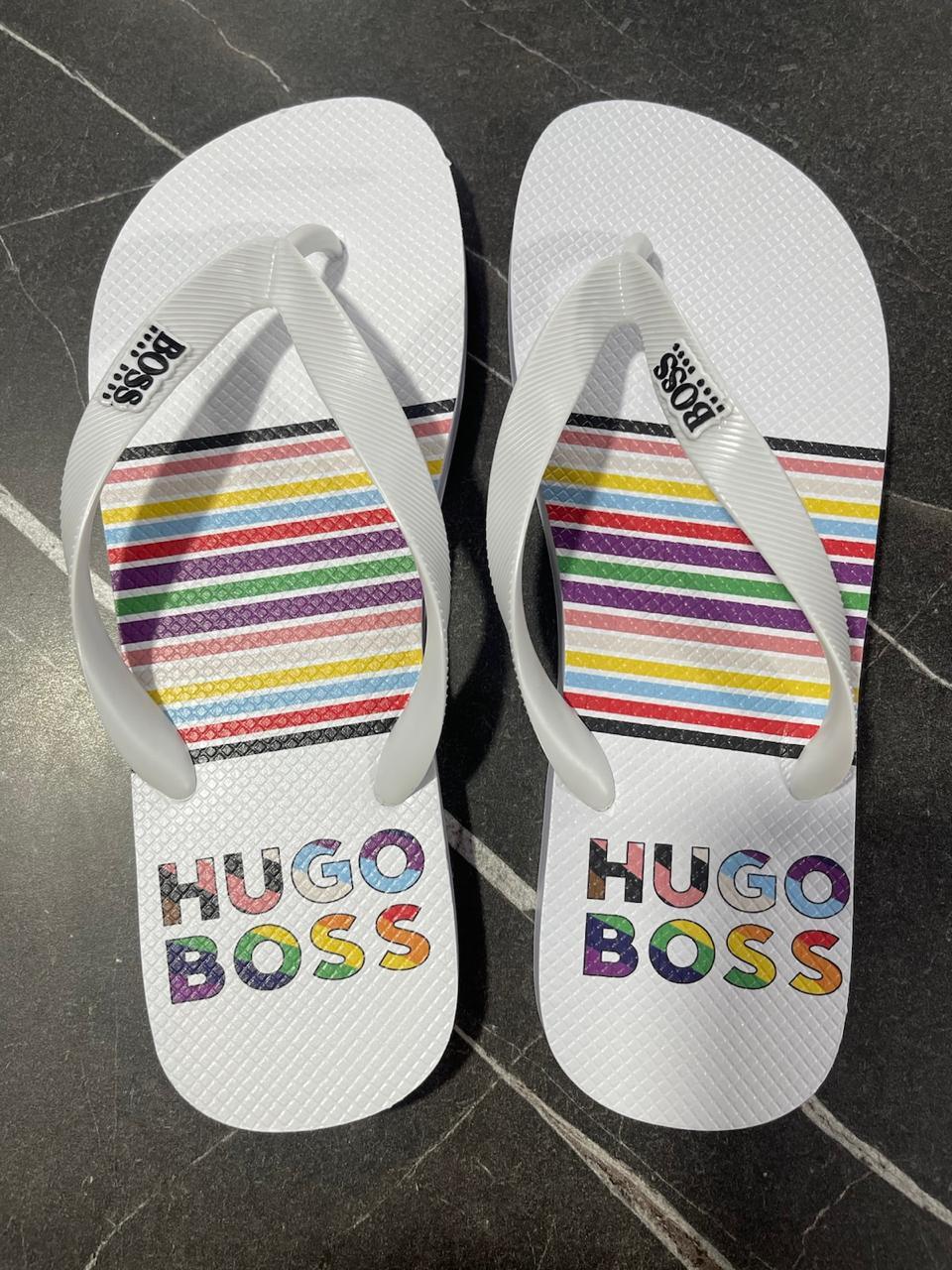 Chinelo Hugo Boss branco com tiras brancas e listras coloridas sobre fundo escuro