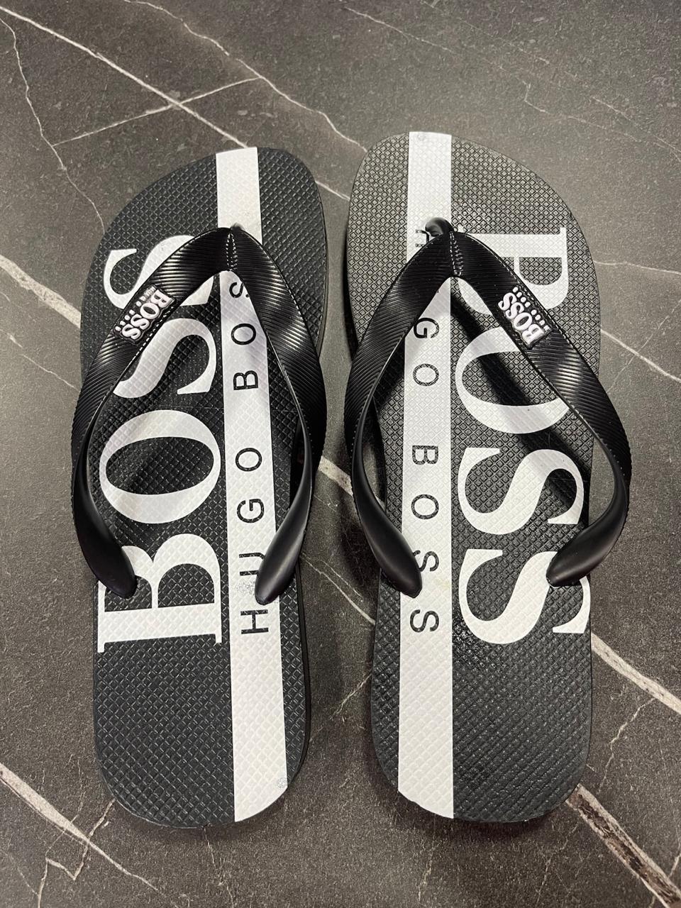 Chinelo Hugo Boss preto com faixa branca e logo grande, em superfície de pedra escura