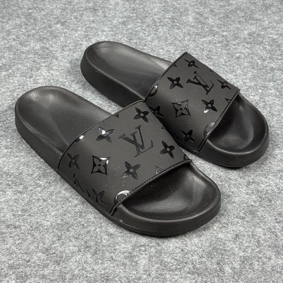 Chinelo slide preto Louis Vuitton com logo e monograma, solado emborrachado, sobre fundo cinza.