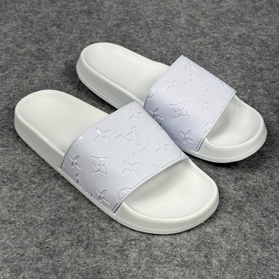 Chinelo branco Louis Vuitton com logo em relevo, sobre fundo de tecido cinza.
