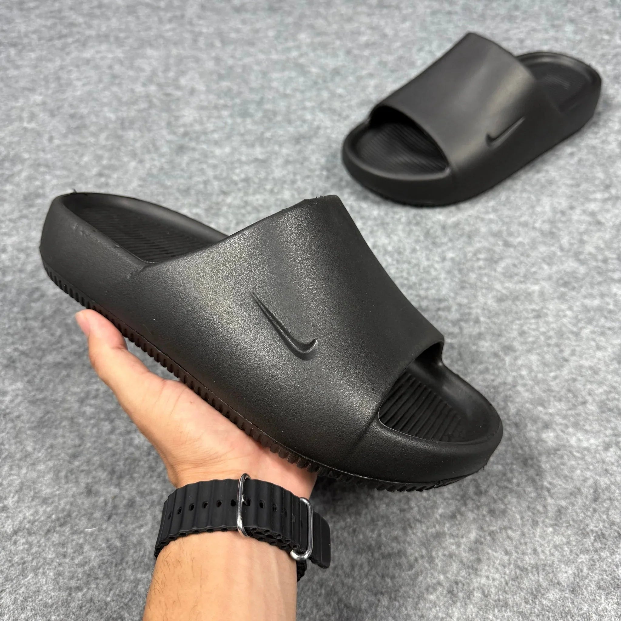 Chinelo Nike Calm Slide preto em destaque sob fundo cinza, design casual e moderno.