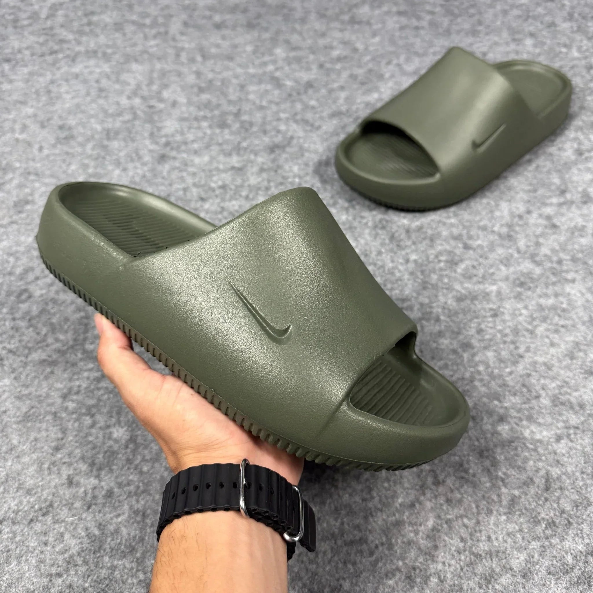 Chinelo Nike Calm Slide verde oliva, sola grossa, logo Nike, em fundo cinza.