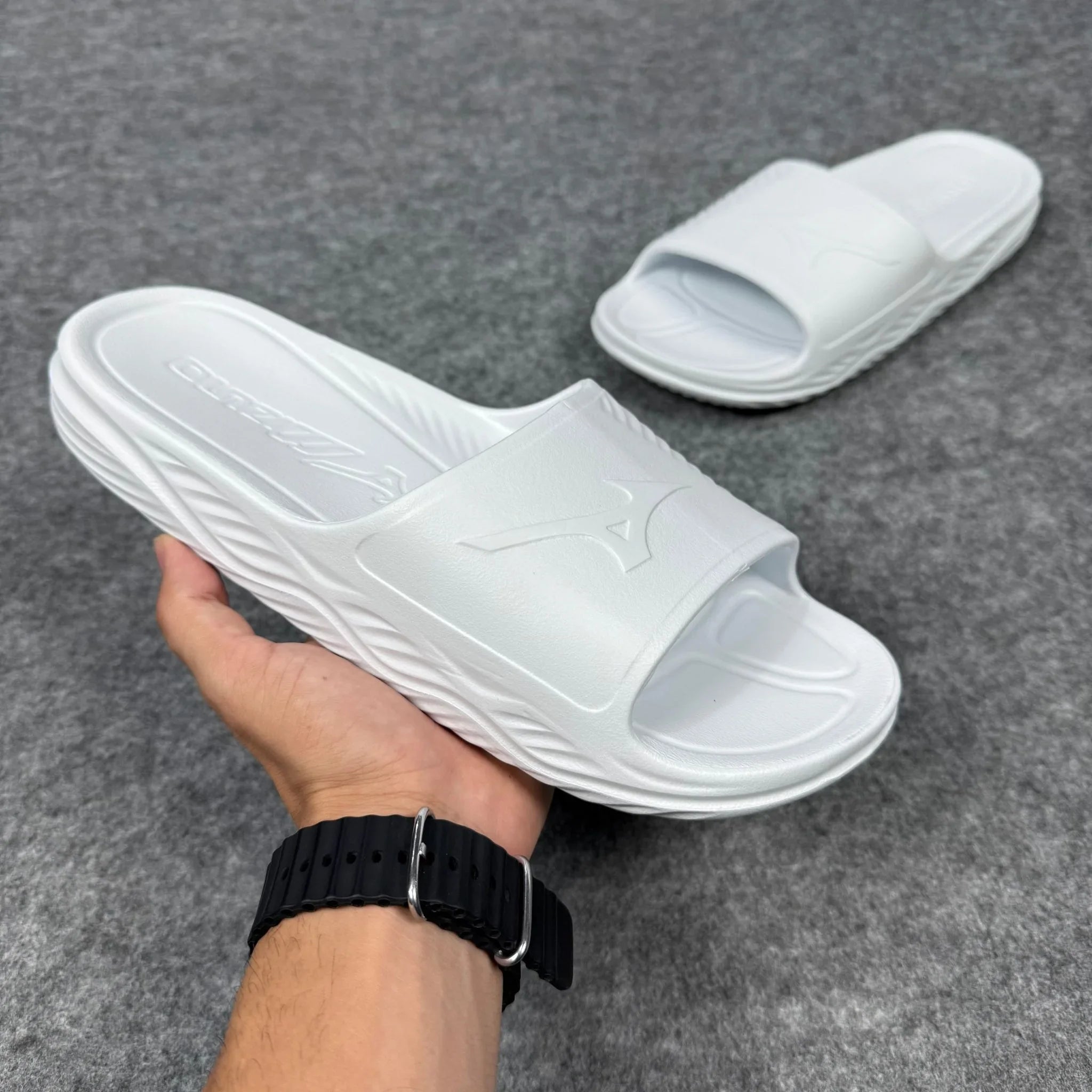 Chinelo slide Mizuno branco com logo em relevo, sola texturizada, em fundo cinza