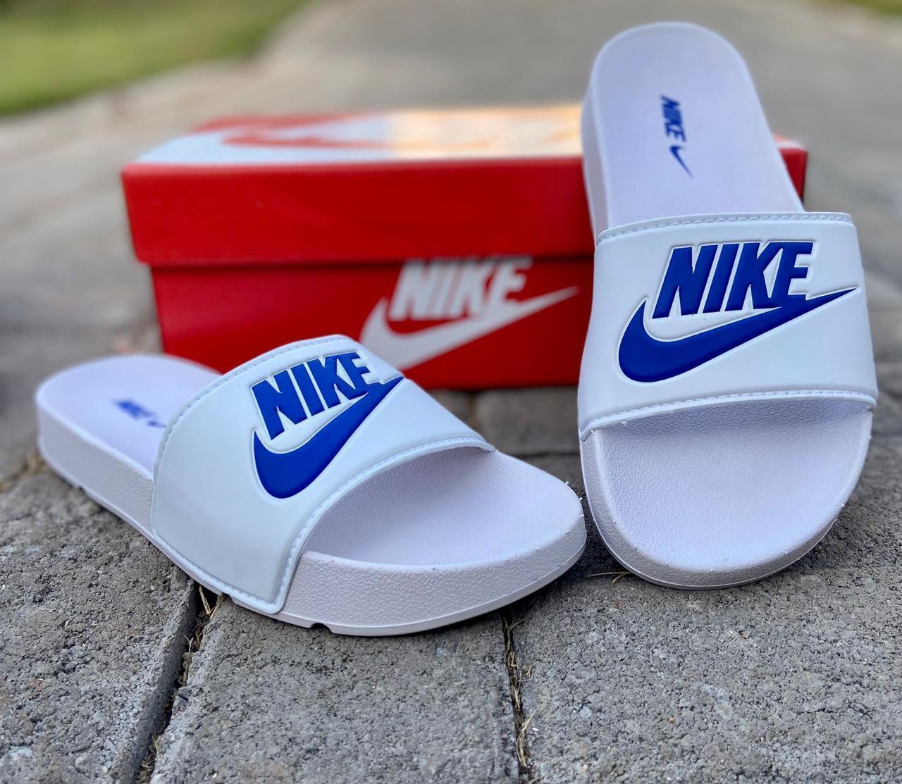 Chinelo slide Nike branco e azul com caixa vermelha sobre piso de pedras