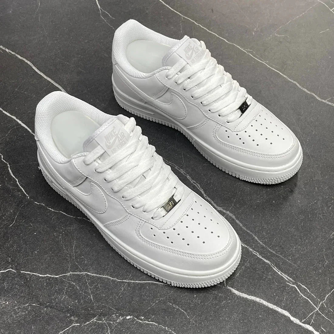 Tênis Nike Air Force 1 branco em couro sobre piso preto marmorizado