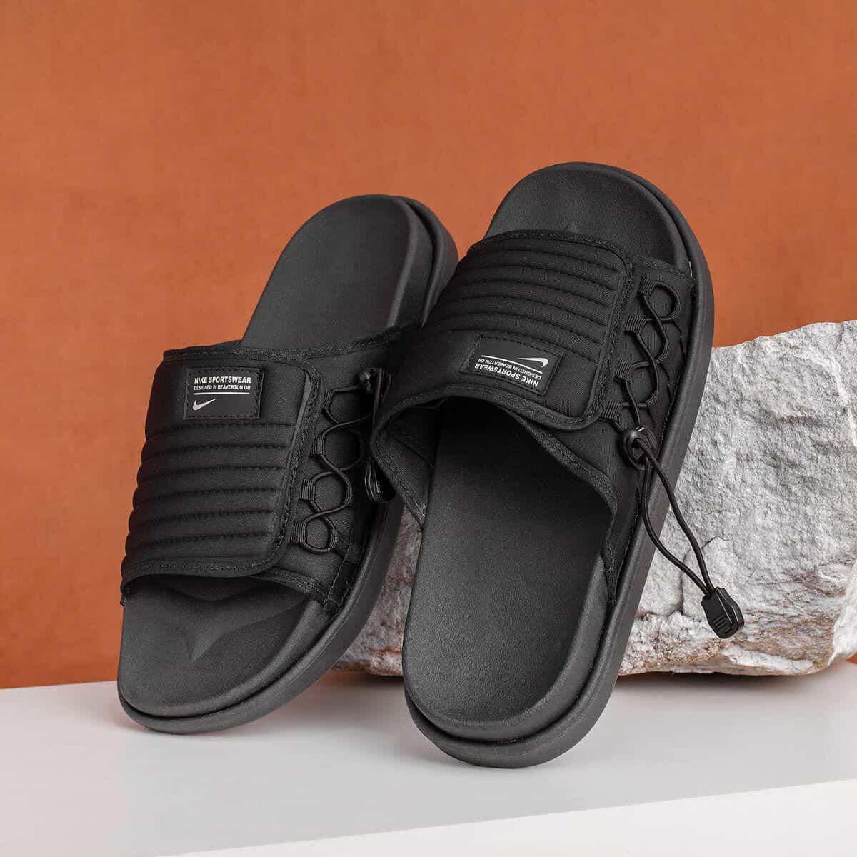 Chinelo Nike Asuna 2 preto esportivo com ajuste, sobre pedra, fundo laranja.