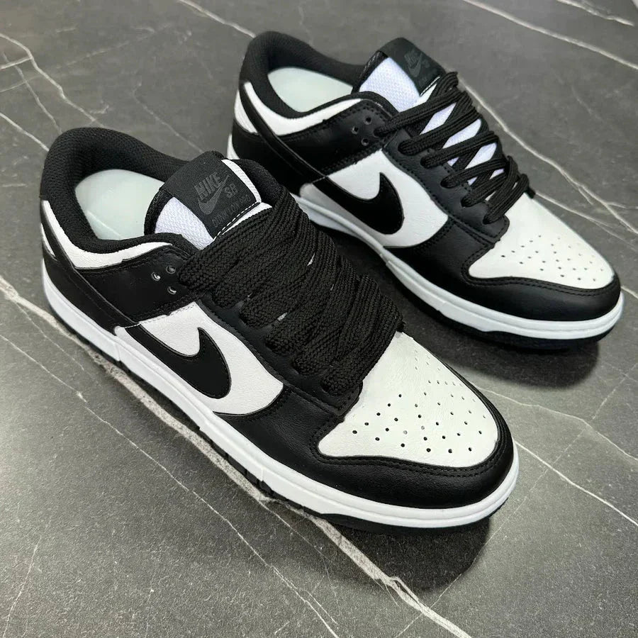 Tênis Nike Dunk Low Panda preto e branco sobre superfície de pedra escura