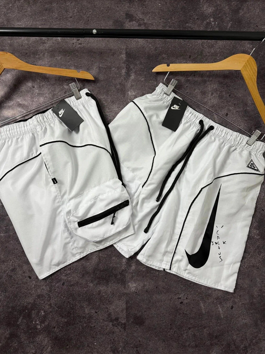 Shorts Nike brancos premium com detalhes pretos, bolsos e logo, em cabides sobre fundo cinza.