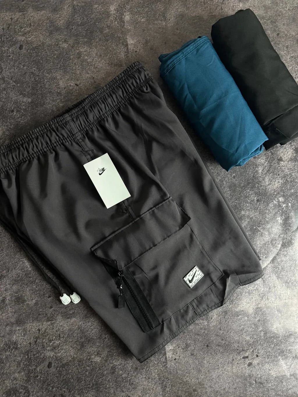 Shorts Nike cargo tactel cinza com bolso utilitário, dobrados em fundo de cimento